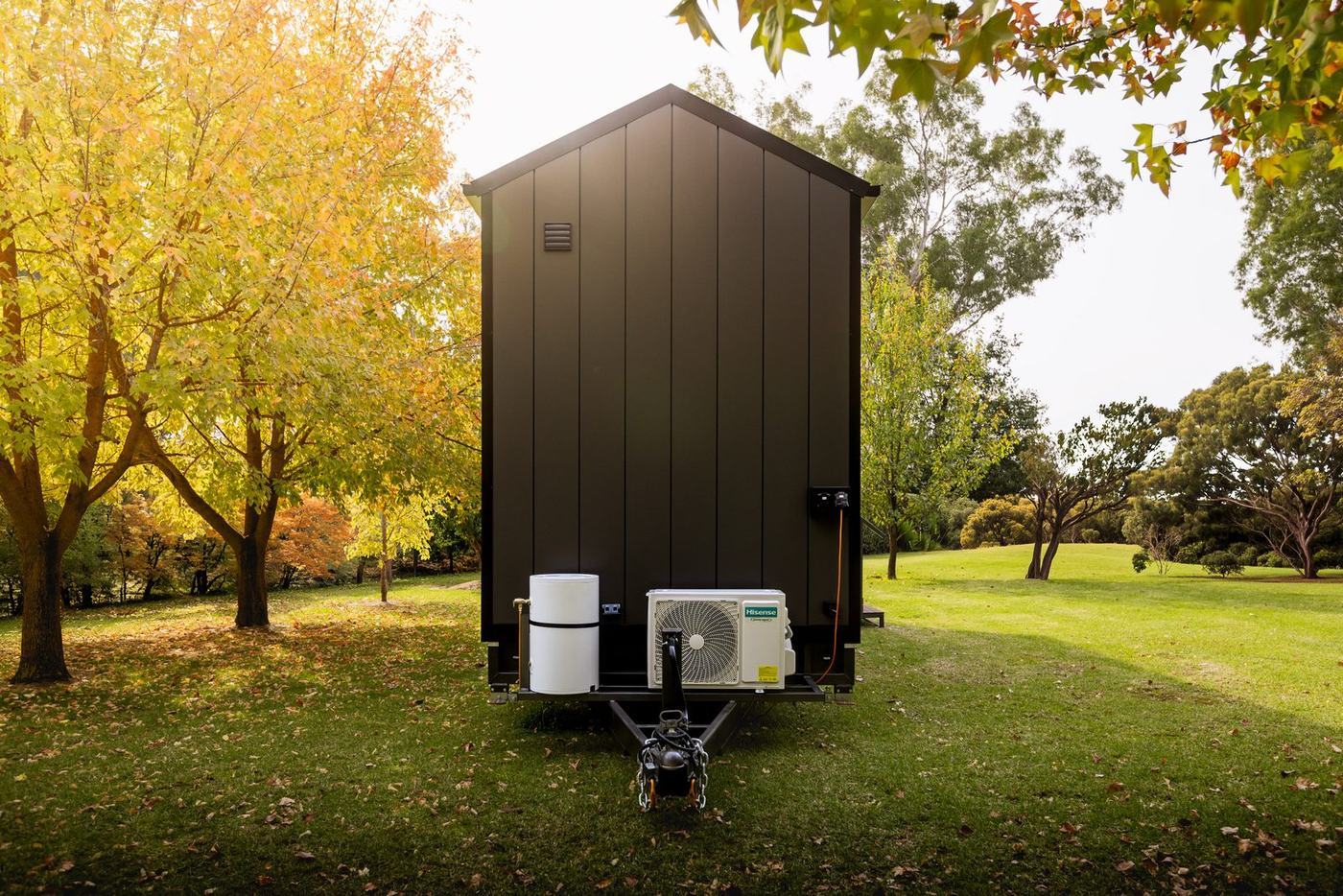 Rear view of the Panarama tiny home showing the tow hitch, hot water unit and air conditioning among autumn trees